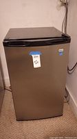 Closed mini beverage fridge with a metallic front and black top and handle, showing the size and exterior condition.
