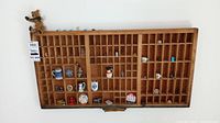 Full view of wooden printers tray filled with small collectibles showing various compartments with individual items including miniature mugs, pins, and figurines.