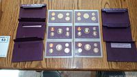 Overview of all three proof sets alongside their original maroon cardboard sleeves placed on a wood table