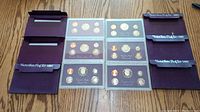 Top view showing three United States Mint proof sets in open maroon holders with original protective cardboard sleeves beside them.
