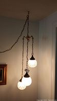 Full view of the vintage hanging light with three illuminated textured glass globes suspended from brass chains.