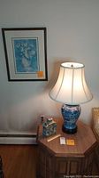 Full view showing wall with floral print, lit lamp on octagon end table, small Asian inspired jar, ruler, and light switches