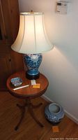 Full view of the table with the lamp on top, small dish on table, and ceramic jar on the floor beside it