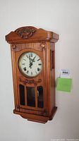 Front view of carved wooden wall clock hanging on wall with closed glass door.