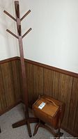 Full view of wooden coat rack with multiple pegs and wooden sewing bin on the floor.