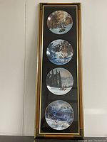 Frontal view of the full framed shadowbox containing the four round collector plates arranged vertically, showcasing detailed nature scenes and gold bamboo trim.
