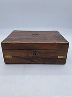 Closed view of the rectangular antique wooden box with brass accents and keyhole on front.