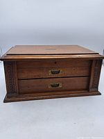 Front view of the closed wooden box showing two drawers, carved columns and brass hardware