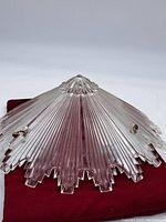 Clear glass Art Deco lamp shade showing the ribbed texture and star shaped edge on a red cloth background.