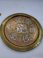 Front view of the brass tray showing silver and copper inlaid Arabic calligraphy and a central geometric motif.