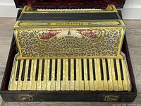 Front view of piano keyboard side showing ivory-tone keys and decorative grille with gold filigree and red accents