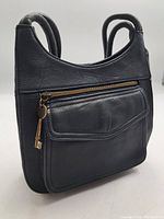 Front angle view of black leather purse showing zippered front pocket with brass zipper and two handles.