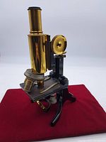 Three-quarter front view of microscope on red cloth showing brass barrel, stage and tripod base