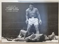 Full view of the black and white Muhammad Ali poster on particleboard showing Ali standing over Liston inside the boxing ring.
