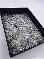 Black container filled with many clear faceted glass beads attached to metal wire loops, viewed at an angle showing bulk quantity.
