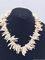 White elongated seashell necklace displayed on black mannequin bust.
