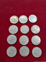 Twelve Canadian silver quarters arranged on red fabric, showing obverse and reverse detail.
