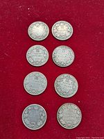Eight Canadian 25 cent silver coins arranged in pairs on red background showing reverse sides with denomination and maple leaf wreath design.