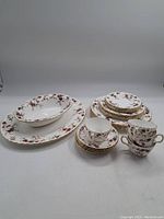 Full laid out dish set with plates, saucers, serving bowl, and serving platter, all showing floral and gold trim design.
