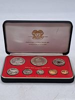 Open black presentation case with seven proof coins mounted in red insert showing various Papua New Guinea animal designs, and interior lid with logo and text
