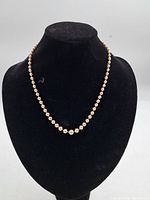 Full view of vintage pearl necklace displayed on black mannequin, showing uniform pearls and overall length.