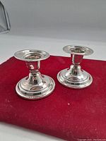 Pair of silver candle holders displayed on a red cloth, showing their shape and reflective surfaces.