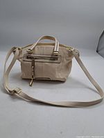 Front view of a small beige Steve Madden purse showing the shape, handles, long strap and front zipper pocket.