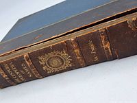Close-up of the spine showing faded gold text The Century Cyclopedia of Names and emblem, with worn leather edges and surface.