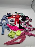 Full lot of vintage Barbie outfits arranged side-by-side on a white surface showcasing various styles and colors.