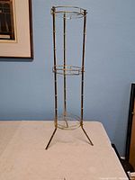 Full view of the tall vintage brass and glass display stand showing its overall structure and tripod legs.