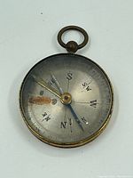 Front view of the vintage compass showing the compass face with cardinal directions, needle, and degree markings. The surface has discoloration near the S direction.