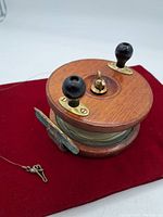 Front side of the vintage wooden fly fishing reel with two black knobs and fishing line attached.