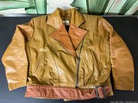 Full view of front of two-tone brown leather jacket showing asymmetrical zipper, wide collar, front zip pockets, and matching belt at waist