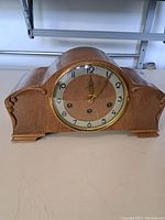 Front view of vintage wooden mantle clock with round dial showing Arabic numerals and gold bezel.