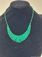 Full view of the necklace on a black bust showing green beads transitioning into tapered rectangular segments.