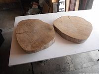 Two hardwood wood disks laid flat on a white table surface, showing the top surfaces with natural wood grain and cracks.