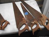 Three vintage hand saws laid side by side on a white table showing wooden handles and rusty blades.