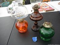 Three vintage oil lamps in green, orange and brown on black table showing general lot contents and colors.
