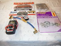 Lot photo showing Classic Cars 2014 calendar, Jaguar E-Type manual, A/C charging adaptor and battery tester on a cloth surface.