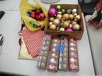 Overview of all Christmas ball ornaments including 4 packages, a cardboard box of assorted balls, and a yellow plastic bag filled with more balls.