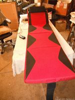 Full length top view of red and black Conair vibrating and heat massage pad laid flat on a table with remote control visible.