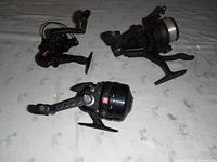 Three fishing reels in a side view showing handle and spool details on a white patterned background.