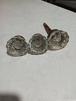Three vintage clear glass door handles with faceted knob design, laid on white surface, showing tops of knobs.