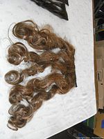 Five auburn wavy hair extensions laid out on a light surface, showing the length and curls.