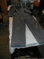 Gray insulated coverall laid flat on a bed, full front view showing long legs and arms, collar, and zipper.