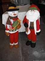 Front view of the snowman and Santa Claus standing side by side on a concrete floor, showing full length and details of clothing and facial features.