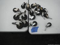Photo showing a variety of caster wheels sized small and large, arranged on a grey table with a blue tape label 'Lot 21'.