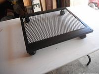 Front/top view of black steel mesh moving dolly on a white table showing mesh platform and caster wheels.