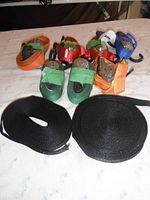 Top view of 7 ratchet straps in orange, green, red, and blue with metal ratchet mechanisms and hooks, alongside two black nylon strapping rolls