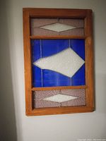 Frontal view of the framed stained glass panel showing the geometric shapes and colored glass within the wood frame.